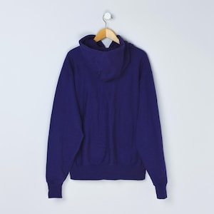 May include: A solid indigo blue hoodie with a hood and long sleeves. The sweatshirt is hanging on a wooden hanger against a white background. The hoodie is made of a soft, thick material.