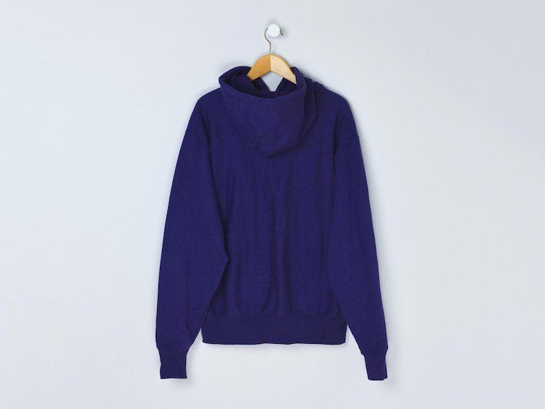 May include: A solid indigo blue hoodie with a hood and long sleeves. The sweatshirt is hanging on a wooden hanger against a white background. The hoodie is made of a soft, thick material.