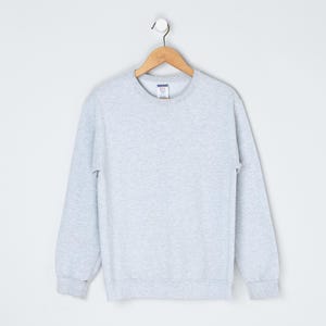 May include: A heather gray sweatshirt with a crew neck and long sleeves. The sweatshirt is hanging on a wooden hanger against a white background. The cuffs and hem are ribbed.