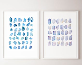 Puede incluir: Dos pinturas al agua enmarcadas con diseños abstractos de círculos azules y morados sobre un fondo blanco. Las pinturas están colgadas en una pared blanca sobre una silla de mimbre con un cojín de hoja verde.