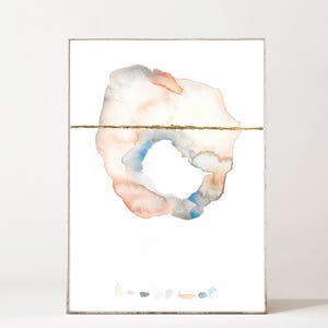 May include: Abstract watercolor art print in a silver frame. The artwork features a circular design with peach, blue, and gray hues, bisected by a gold line. Small, colorful shapes are at the bottom.