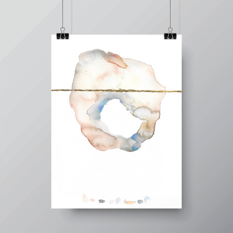May include: Abstract watercolor art print featuring a soft, organic shape in muted tones of peach, gray, and blue, bisected by a thin, gold horizontal line. The artwork is displayed on white paper, held by black binder clips.