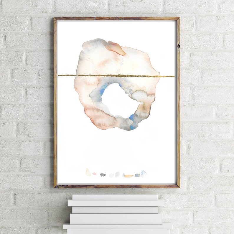 May include: Abstract watercolor art print in a wooden frame. The artwork features a circular shape with a gold horizontal line, and a palette of soft colors including peach, blue, and gray. The print is displayed on a white background.