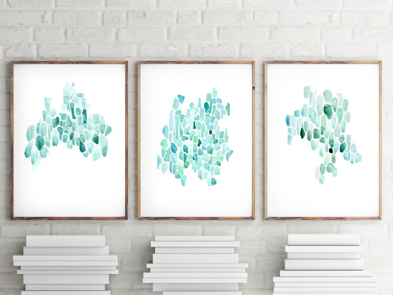 May include: Three framed watercolor paintings with abstract designs in shades of blue and green. The designs are made up of small, irregular shapes that resemble sea glass.