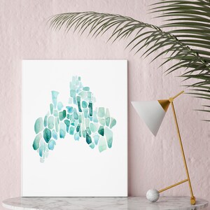 May include: A framed abstract watercolor painting with a teal and blue color scheme. The painting is made up of many small, irregular shapes that resemble pebbles or stones. The painting is displayed on a white marble table with a gold lamp.