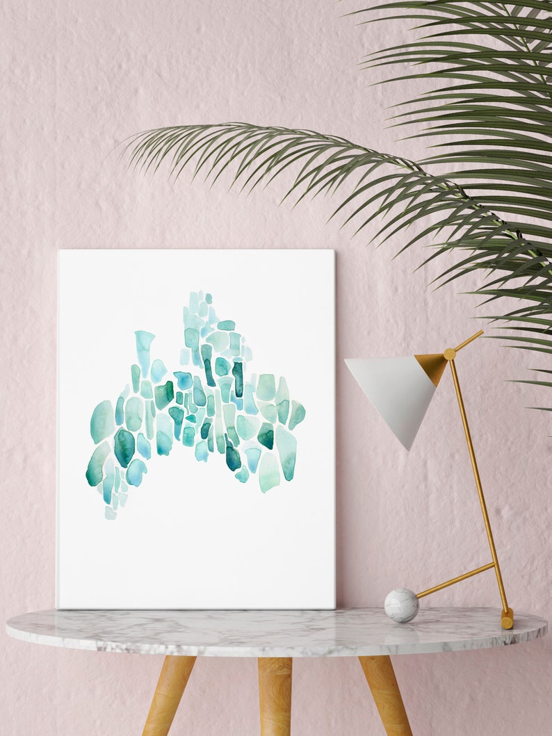 May include: A framed abstract watercolor painting with a teal and blue color scheme. The painting is made up of many small, irregular shapes that resemble pebbles or stones. The painting is displayed on a white marble table with a gold lamp.