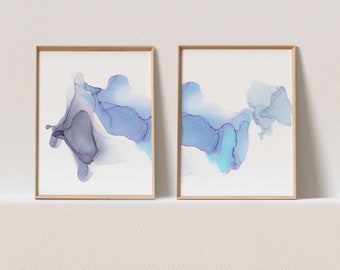 Puede incluir: Dos impresiones de arte abstracto enmarcadas con diseños azul y morado como acuarela sobre un fondo blanco.