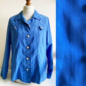 Könnte beinhalten: Eine blaue Wildlederjacke mit Knopfleiste und langen Ärmeln. Die Jacke hat zwei Brusttaschen und einen Kragen.