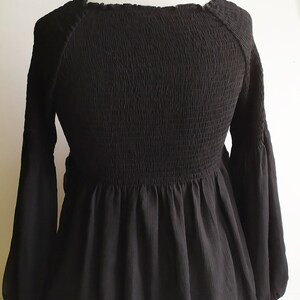 May include: A black, long-sleeved blouse with a smocked bodice and a ruffled hem.