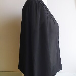 May include: A black sheer blouse with a lace trim around the neckline and a gathered elastic band at the bottom of the sleeves. The blouse has a v-neckline and a button closure at the front.