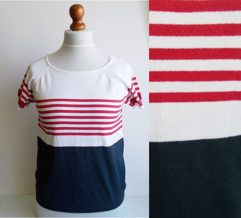 K&ouml;nnte beinhalten: Ein wei&szlig;- und marineblaues, kurz&auml;rmeliges Shirt mit roten Streifen. Das Shirt hat einen runden Ausschnitt und eine lockere Passform.