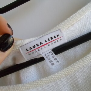 K&ouml;nnte beinhalten: Wei&szlig;er Pullover mit einem wei&szlig;en Etikett mit der Aufschrift "LAURA LEBEK MODERN WOMAN" und Gr&ouml;&szlig;enangaben in verschiedenen Gr&ouml;&szlig;ensystemen.