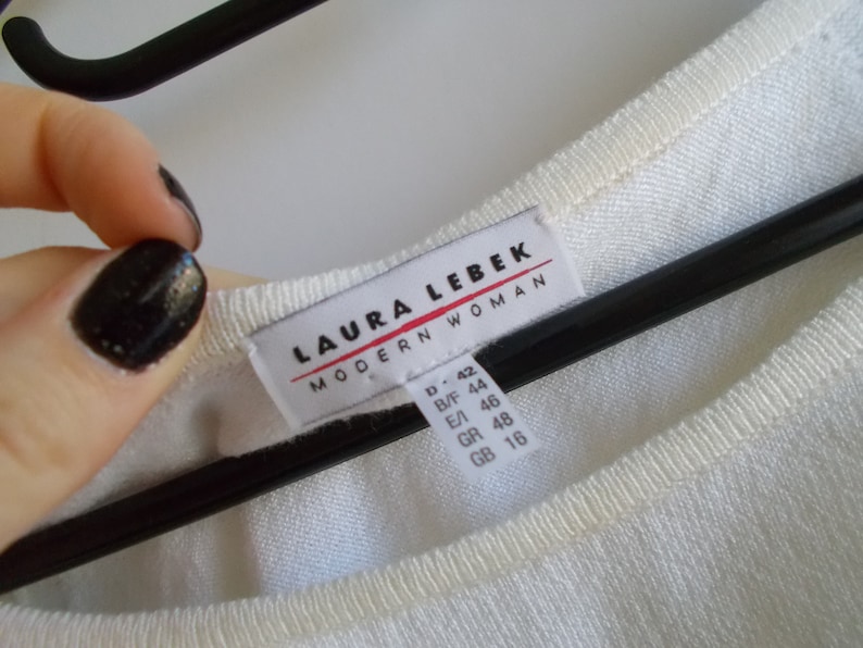 K&ouml;nnte beinhalten: Wei&szlig;er Pullover mit einem wei&szlig;en Etikett mit der Aufschrift "LAURA LEBEK MODERN WOMAN" und Gr&ouml;&szlig;enangaben in verschiedenen Gr&ouml;&szlig;ensystemen.