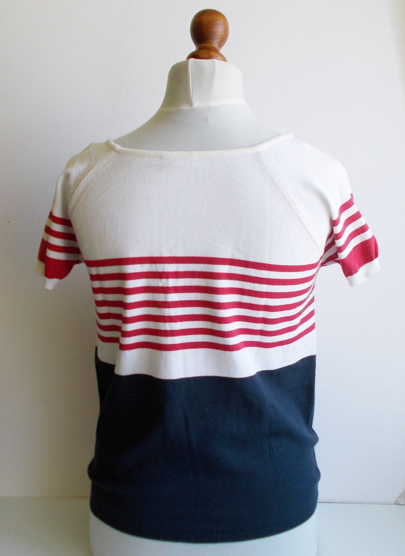 K&ouml;nnte beinhalten: Ein wei&szlig;-marineblaues, kurz&auml;rmeliges Shirt mit roten Streifen.
