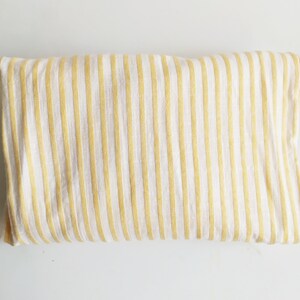 May include: A white fabric with yellow stripes. The fabric is folded in half and laid flat on a white surface.