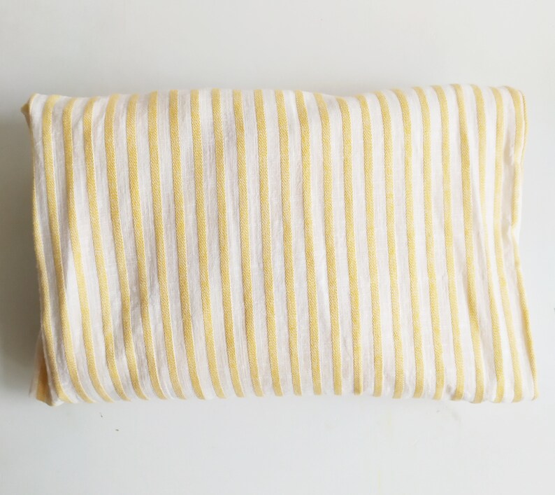 May include: A white fabric with yellow stripes. The fabric is folded in half and laid flat on a white surface.