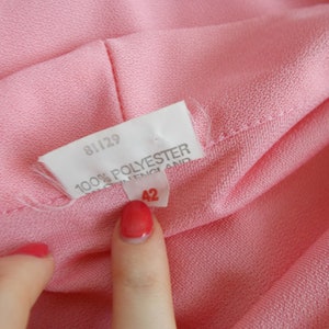 May include: Close-up of a pink fabric label with the text "81129 100% POLYESTER MADE IN ENGLAND 42" printed on it.