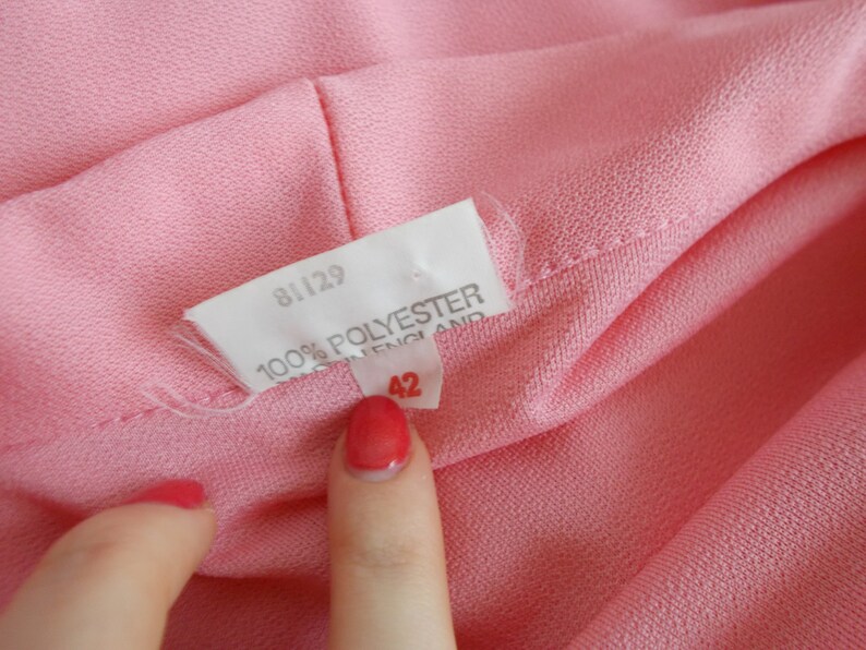 May include: Close-up of a pink fabric label with the text "81129 100% POLYESTER MADE IN ENGLAND 42" printed on it.