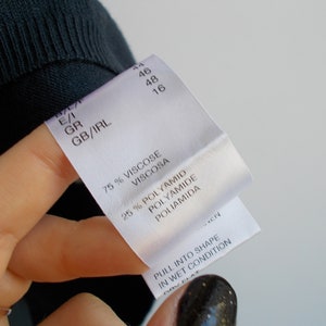 K&ouml;nnte beinhalten: Wei&szlig;es Kleidungsetikett mit schwarzem Text. Das Etikett lautet "75% Viskose Viscosa 25% Polyamid Polyamide Poliamida". Das Etikett lautet auch "Pull into shape in wet condition".