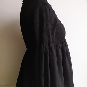 May include: A black, sheer, smocked top with a loose, flowing silhouette. The top has a V-neckline and long sleeves.