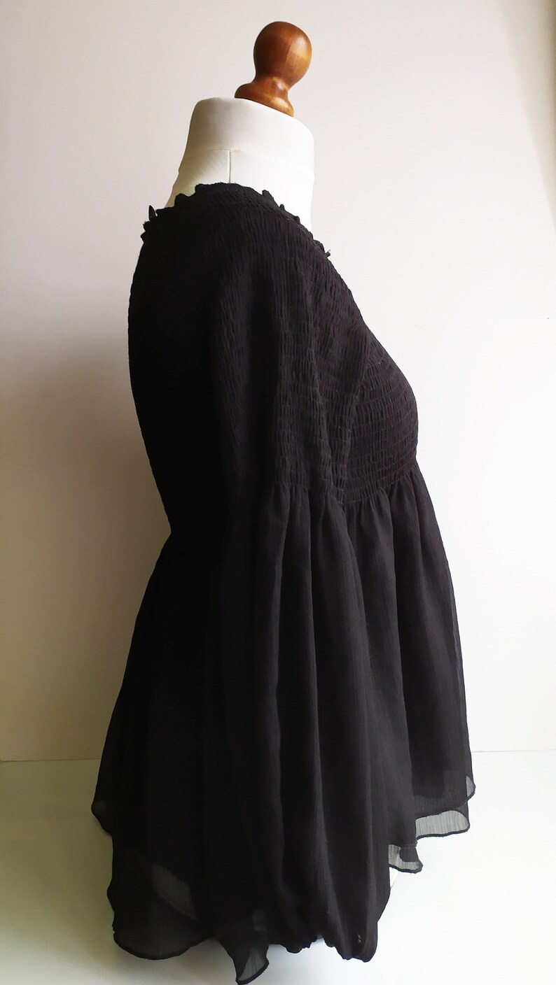 May include: A black, sheer, smocked top with a loose, flowing silhouette. The top has a V-neckline and long sleeves.