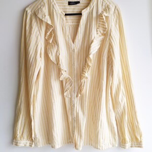 May include: A yellow and white striped long-sleeved blouse with a ruffled neckline. The blouse has a button-up front.