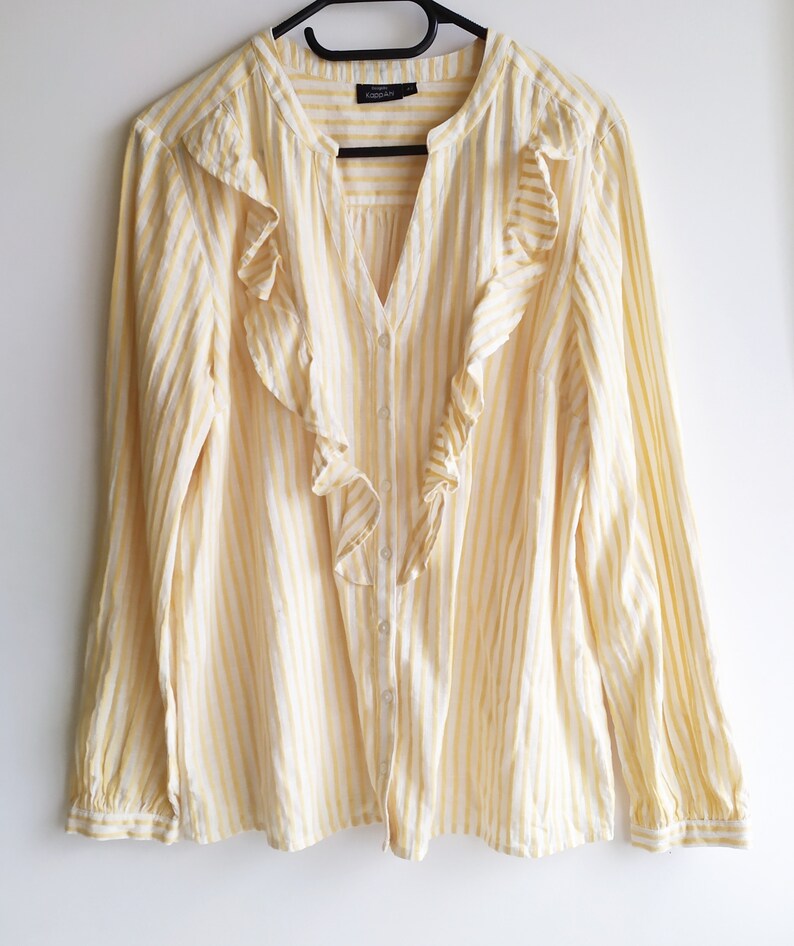 May include: A yellow and white striped long-sleeved blouse with a ruffled neckline. The blouse has a button-up front.