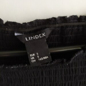 May include: Black clothing tag with white text that reads "LINDEX" and size information: EUR S, UK S, CN 165/88A.
