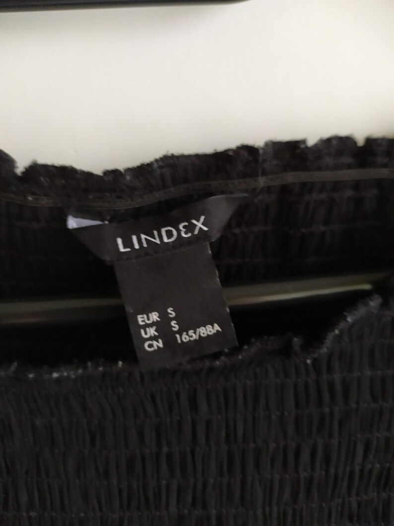 May include: Black clothing tag with white text that reads "LINDEX" and size information: EUR S, UK S, CN 165/88A.