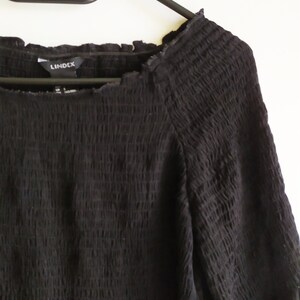 May include: Black, long-sleeved, off-the-shoulder dress with a smocked bodice and a ruffled hem. The dress has a "Lindex" brand label.