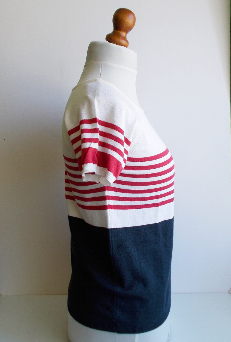 K&ouml;nnte beinhalten: Ein wei&szlig;-rot gestreiftes Kurzarm-Shirt mit einem dunkelblauen Saum.