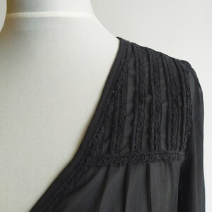 May include: Black sheer blouse with a V-neckline and lace trim detail on the shoulders.