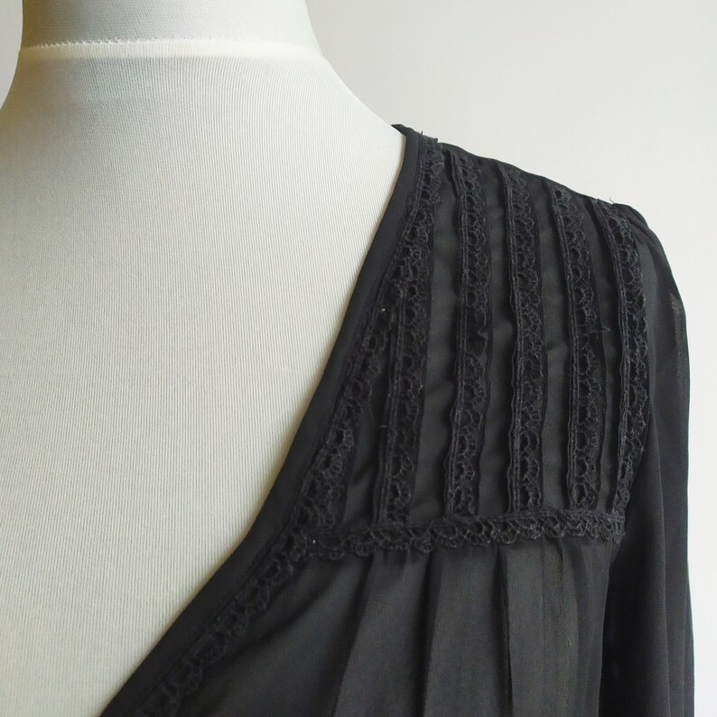 May include: Black sheer blouse with a V-neckline and lace trim detail on the shoulders.