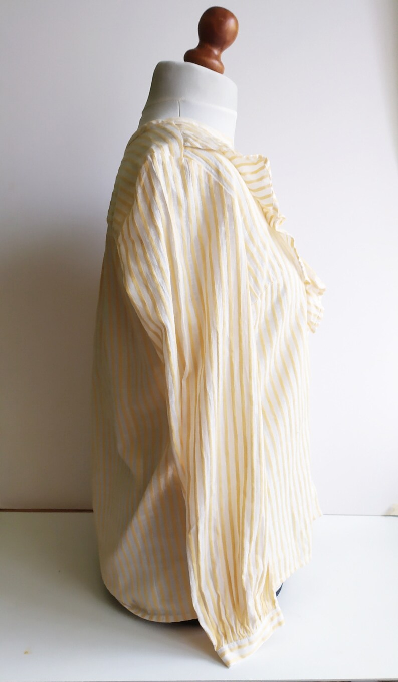 May include: A white and yellow striped long-sleeve blouse with a ruffled collar.