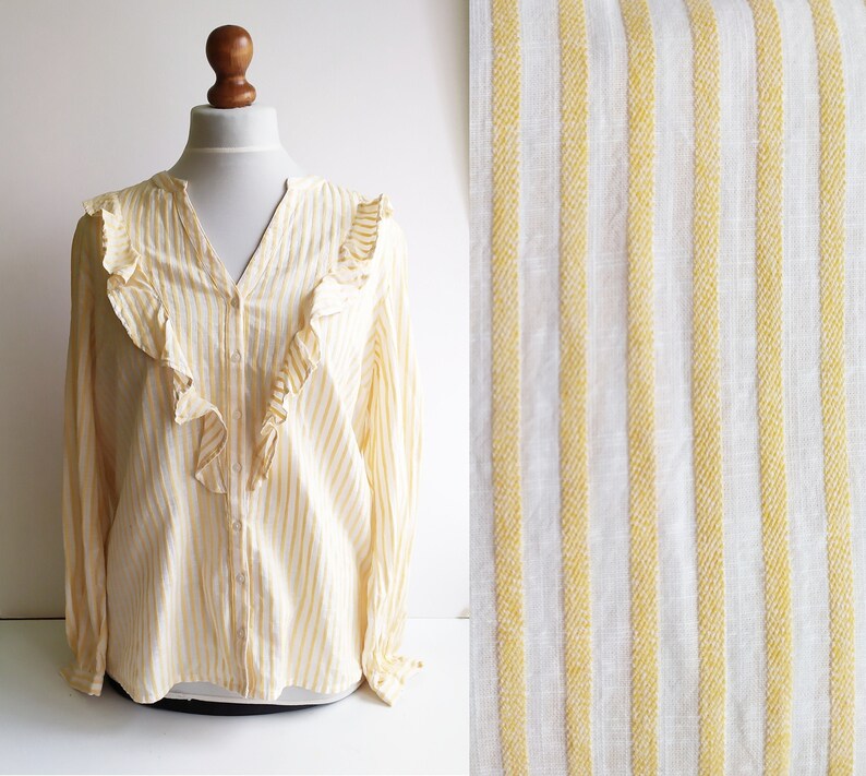 May include: A yellow and white striped long-sleeved blouse with a ruffled neckline. The blouse has a button-up front and is made of a lightweight fabric.