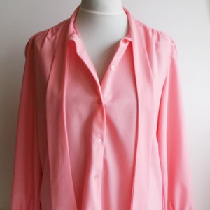 May include: A pink long-sleeved blouse with a tie at the neck and button closure.