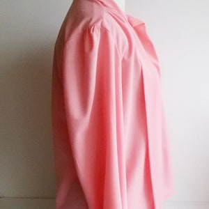 May include: A pink long-sleeved blouse with a gathered neckline and a button closure. The blouse is made of a lightweight fabric and has a relaxed fit.