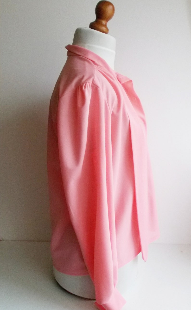 May include: A pink long-sleeved blouse with a gathered neckline and a button closure. The blouse is made of a lightweight fabric and has a relaxed fit.