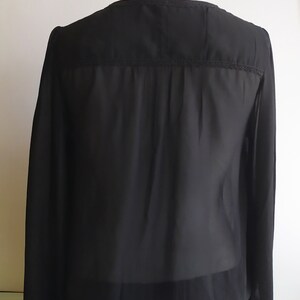May include: A black sheer long-sleeved blouse with a lace trim around the neckline and cuffs.