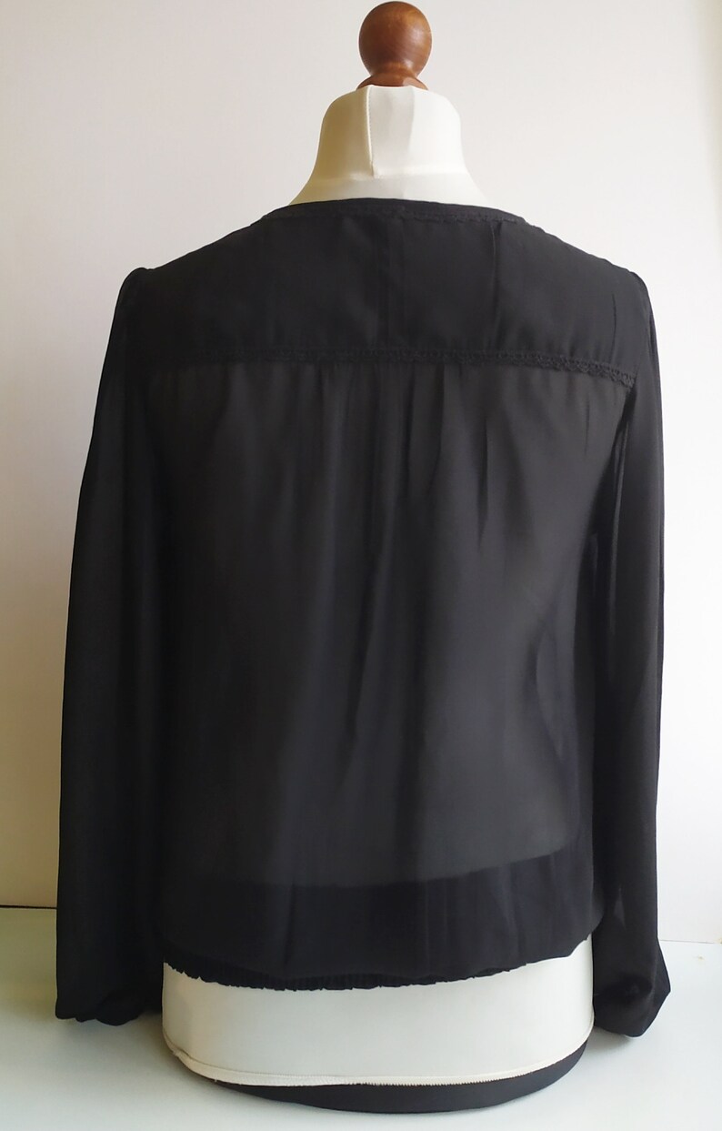 May include: A black sheer long-sleeved blouse with a lace trim around the neckline and cuffs.