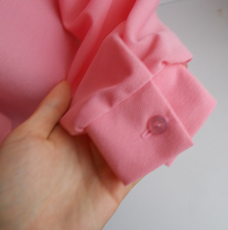 May include: Close-up of a pink long-sleeved shirt with a button on the cuff.