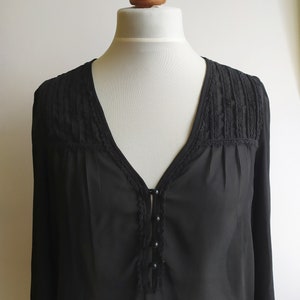 May include: A black sheer blouse with a V-neckline and lace trim. The blouse has a button closure and long sleeves.