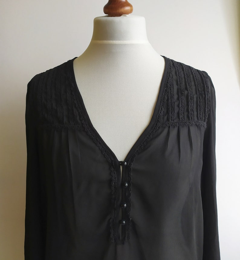 May include: A black sheer blouse with a V-neckline and lace trim. The blouse has a button closure and long sleeves.