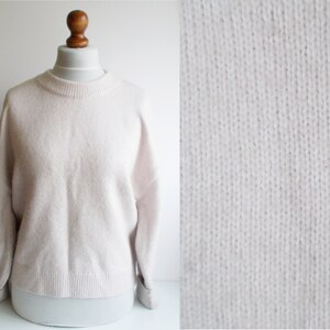 Può includere: Un maglione di lana bianco morbido con collo rotondo e maniche lunghe.