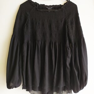 May include: Black long-sleeve blouse with a gathered, ruffled neckline and a tiered, ruffled hem. The blouse has a relaxed fit and is made of a lightweight, sheer fabric.