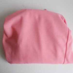 May include: A pink fabric pouch or bag, folded and lying flat on a white surface.