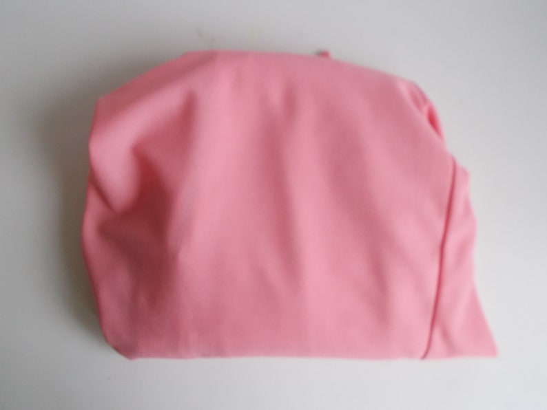 May include: A pink fabric pouch or bag, folded and lying flat on a white surface.