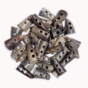 May include: A pile of brown and black horn buttons with two or three holes each. The buttons are shaped like a pointed oval.
