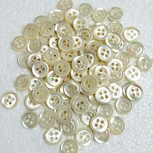 Può includere: Un grande mucchio di bottoni rotondi di madreperla bianca con quattro fori ciascuno.