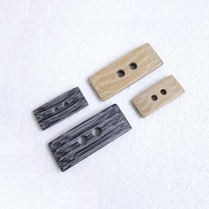 May include: Four rectangular buttons with two holes each. Two buttons are light brown with a wood grain pattern, and two buttons are black with a white stripe pattern.